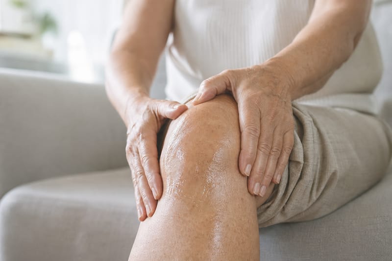 Donna seduta sul divano che massaggia il gel sul ginocchio con entrambe le mani